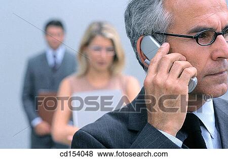 Businessman talking on a cell phone, two businesspeople in the background, blurred View Large Photo Image Stock Photo - Businessman talking on a cell phone, two businesspeople in the background, blurred. Fotosearch