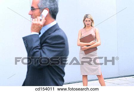 Businessman talking on cell phone, businesswoman in the background looking at camera View Large Photo Image Stock Image - Businessman talking on cell phone, businesswoman in the background looking at camera. Fotosearch