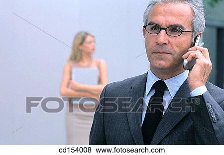 Businessman talking on cell phone, businesswoman in the background View Large Photo Image Stock Photo - Businessman talking on cell phone, businesswoman in the background. Fotosearch
