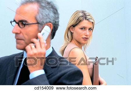 Businessman talking on cell phone, businesswoman in the background looking at camera View Large Photo Image Stock Photo - Businessman talking on cell phone, businesswoman in the background looking at camera. Fotosearch