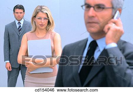 Businessman talking on cell phone, two businesspeople in the background looking at camera View Large Photo Image Stock Photograph - Businessman talking on cell phone, two businesspeople in the background looking at camera. Fotosearch