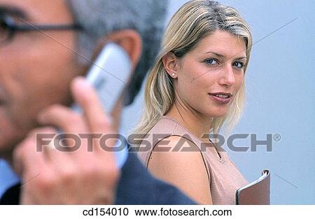 Businessman with cell phone in front, businesswoman in the background looking at camera View Large Photo Image Stock Image - Businessman with cell phone in front, businesswoman in the background looking at camera. Fotosearch