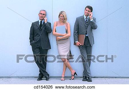 Stock Photograph - Two businessmen talking on cell phone, woman waiting. Fotosearch