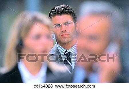 Two businesspeople talking on cell phones in the front, man waiting in the background View Large Photo Image Stock Photo - Two businesspeople talking on cell phones in the front, man waiting in the background. Fotosearch