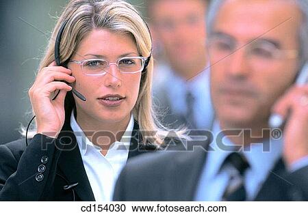 Stock Image - Two executives talking on cell phones, one man standing in the background. Fotosearch