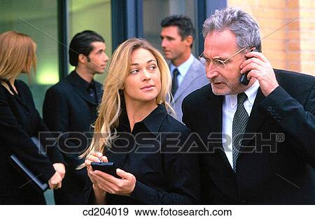 Stock Photo - Businessman talking on cell phone, businesswoman with organizer, three businesspeople in the background. Fotosearch