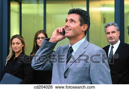 Businessman talking on cell phone, businesspeople in the background View Large Photo Image Stock Photograph - Businessman talking on cell phone, businesspeople in the background. Fotosearch