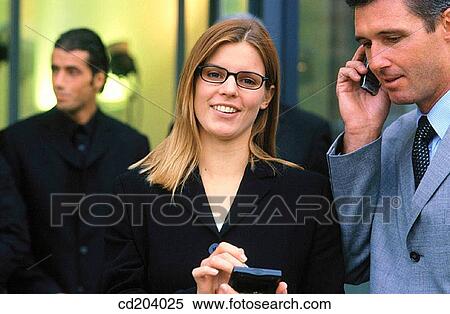 Businesswoman looking at camera, businessman talking on cell phone View Large Photo Image Stock Photography - Businesswoman looking at camera, businessman talking on cell phone. Fotosearch