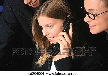 Businesswoman talking on phone, two businesspeople in the background looking interested View Large Photo Image Picture - Businesswoman talking on phone, two businesspeople in the background looking interested. Fotosearch