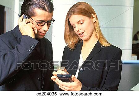 Businesswoman working with personal organizer, businessman talking on cell phone View Large Photo Image Stock Photography - Businesswoman working with personal organizer, businessman talking on cell phone. Fotosearch