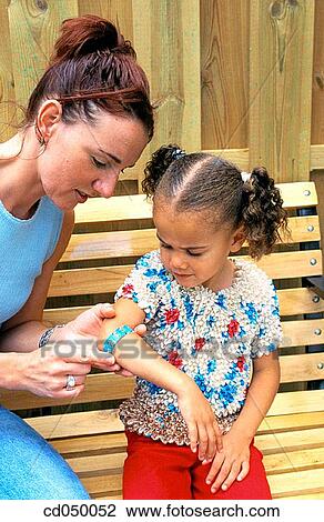 Stock Image - Mother putting adhesive bandage on her daughter's arm. Fotosearch