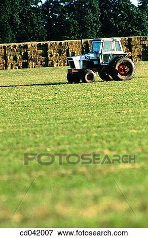 Tractor in field, bales of hay in distance View Large Photo Image Stock Photo - Tractor in field, bales of hay in distance. Fotosearch
