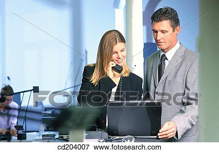 Two businesspeople in front of laptop, businesswoman talking on phone View Large Photo Image Stock Photo - Two businesspeople in front of laptop, businesswoman talking on phone. Fotosearch