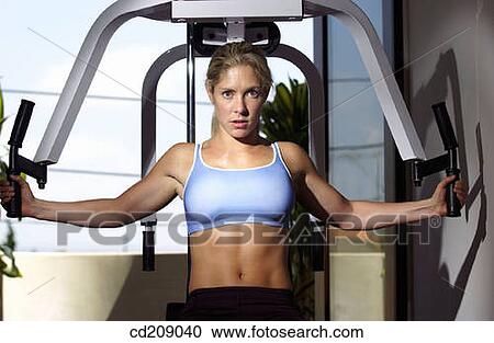 Stock Image - Woman working out by weight lifting on a home gym. Fotosearch