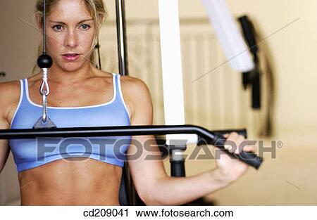 Stock Image - Woman working out by weight lifting on a home gym. Fotosearch