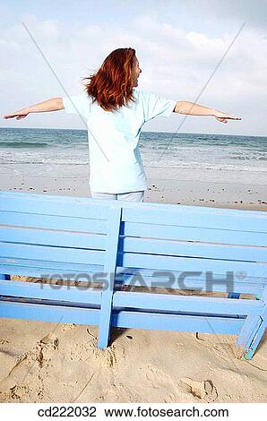 Stock Image - blue, Arms raised, bench, beach, back view, anonymous. Fotosearch