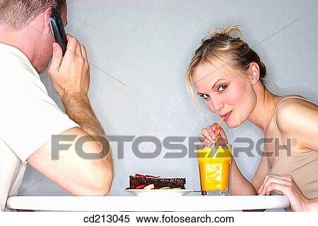 Woman drinking orange juice with man talking mobile phone View Large Photo Image Stock Photography - Woman drinking orange juice with man talking mobile phone. Fotosearch