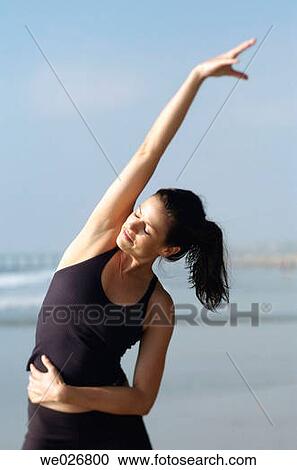 Stock Image - A woman stretching and getting ready to run on the beach.. Fotosearch