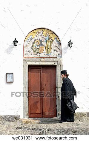 Stock Image - A Greek Orthodox priest at the entrance to the Monastery of the Apocalypse on the island of Patmos, Greece.. Fotosearch