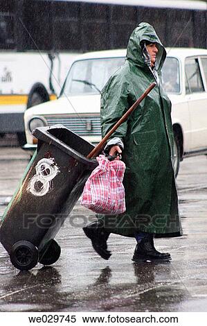 Street sweeper carrying a garbage bin in front of the Bucharest North Railway Station. Attached to her bin, a bag can be noticed - it is in there she collects things from the garbage that might be useful at her home View Large Photo Image Stock Photography - Street sweeper carrying a garbage bin in front of the Bucharest North Railway Station. Attached to her bin, a bag can be noticed - it is in there she collects things from the garbage that might be useful at her home. Fotosearch