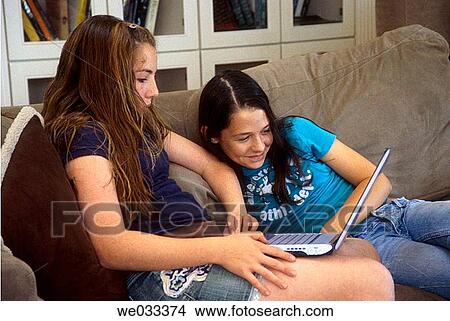 Teenage girls using a laptop while on a couch in a living room View Large Photo Image Picture - Teenage girls using a laptop while on a couch in a living room. Fotosearch