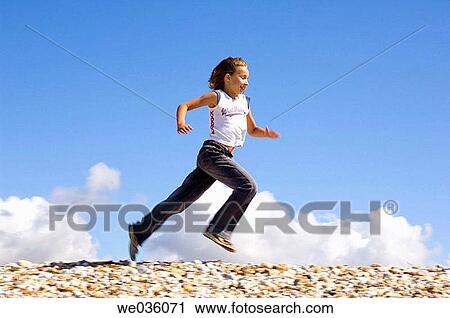 Stock Image - Girl running along pebbly levee. Fotosearch