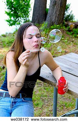Stock Image - Teenage girl, sitting at a picnic table, blowing soap bubbles. Fotosearch