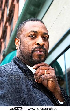 Young black man, with his hand under his chin, standing on a downtown city street View Large Photo Image Stock Image - Young black man, with his hand under his chin, standing on a downtown city street. Fotosearch