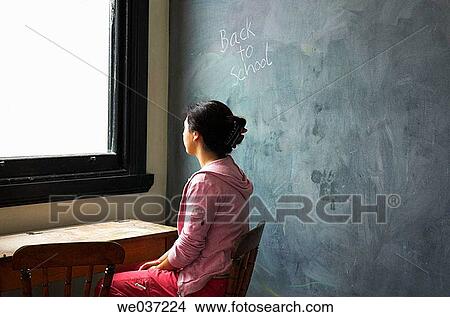 Young woman sitting at old school desk with blackboard behind her and the words? back to school? on board. View Large Photo Image Picture - Young woman sitting at old school desk with blackboard behind her and the words? back to school? on board.. Fotosearch