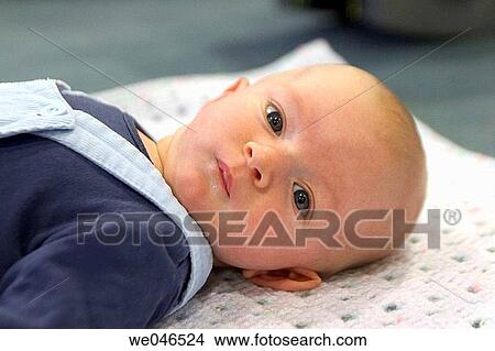 Picture - 2 month old baby boyl lying on his back, with big blue eyes looking into camera. Fotosearch
