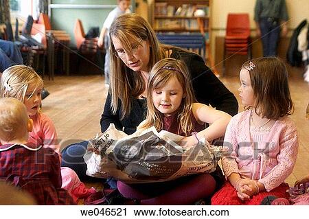 Stock Image - 4 year old girl at a children party opening a present in pass the parcel, sitting on her mothers knees.. Fotosearch