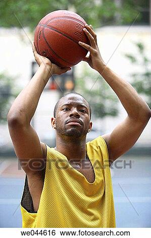 Stock Photograph - African-American man holding a basketball over his head and looking into camera. Fotosearch