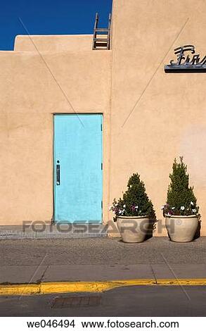 An empty sidewalk and potted trees by a closed blue door of an adobe building in Taos, New Mexico, USA. View Large Photo Image Picture - An empty sidewalk and potted trees by a closed blue door of an adobe building in Taos, New Mexico, USA.. Fotosearch