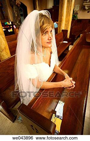 Stock Photograph - Bride kneeling and praying in a church pew. Fotosearch