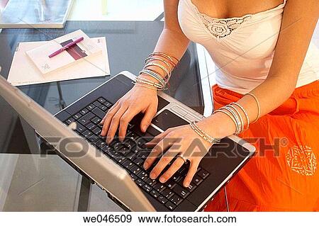 Stock Photo - Closeup of girls hands on a laptop, wearing lots of bangles.. Fotosearch