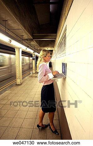 Woman working on laptop in subway station against wall View Large Photo Image Stock Image - Woman working on laptop in subway station against wall. Fotosearch