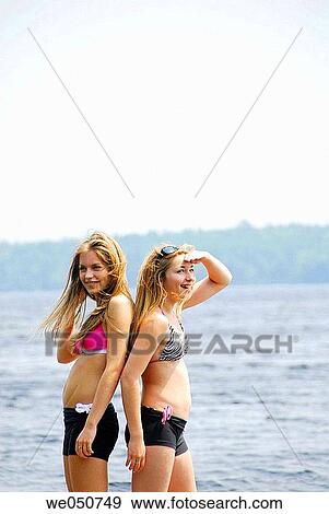 Stock Photo - 13 yr old and 18 yr old sisters standing on dock looking out. Fotosearch
