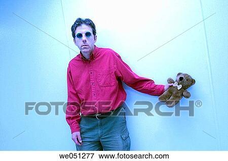 Middle-age man, wearing sunglasses and standing by a wall, holding a stuffed teddy bear View Large Photo Image Stock Photo - Middle-age man, wearing sunglasses and standing by a wall, holding a stuffed teddy bear. Fotosearch