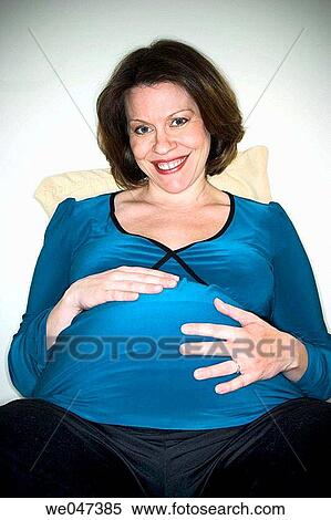 Pregnant woman sitting on her bed, her hands on her belly View Large Photo Image Stock Photography - Pregnant woman sitting on her bed, her hands on her belly. Fotosearch