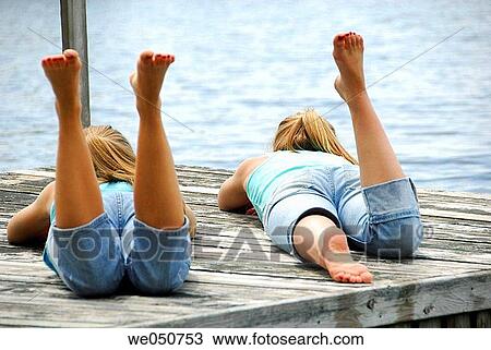 Stock Image - sisters 13 and 18 yrs laying on dock. Fotosearch