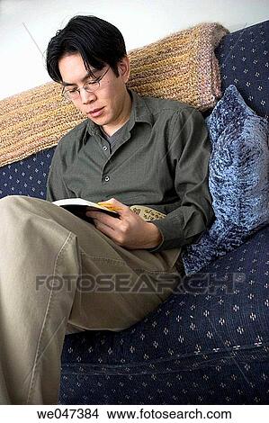 Young Asian man, wearing glasses and sitting on his sofa, reading a book View Large Photo Image Picture - Young Asian man, wearing glasses and sitting on his sofa, reading a book. Fotosearch