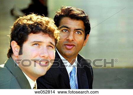 2 young male business men sitting together looking up at office building View Large Photo Image Picture - 2 young male business men sitting together looking up at office building. Fotosearch
