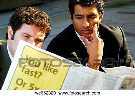 Stock Image - 2 young male business men sitting together reading paper. Fotosearch