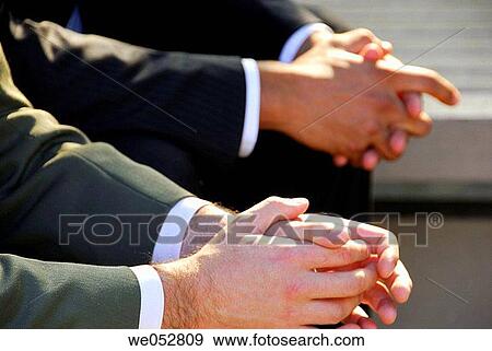 Stock Photo - 2 young male business men sitting outdoors with hands folded rested on knees. Fotosearch