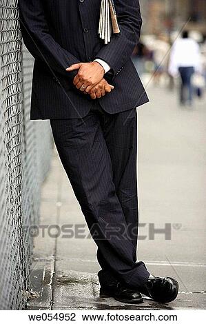 Business man with paper under arm leaning on fence neck down View Large Photo Image Stock Image - Business man with paper under arm leaning on fence neck down. Fotosearch