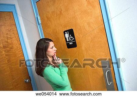 Young woman standing next to a men's bathroom View Large Photo Image Picture - Young woman standing next to a men's bathroom. Fotosearch