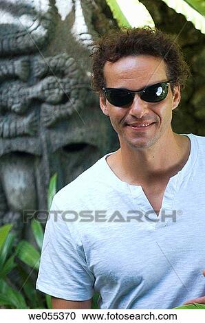 Stock Image - man posing with primitive mask in the background. Fotosearch