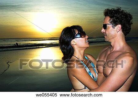 young couple embracing on the beach with sunset in the background View Large Photo Image Stock Photography - young couple embracing on the beach with sunset in the background. Fotosearch