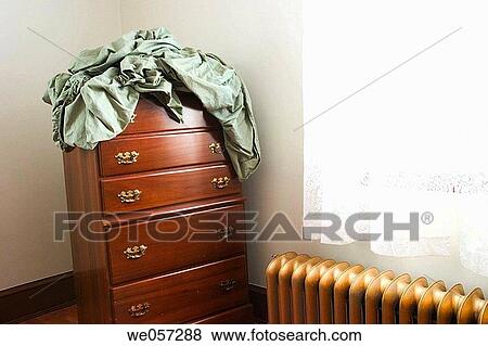 Bedsheets setting on top of a bureau, which is next to a window and a gold_colored iron radiator View Large Photo Image Stock Photo - Bedsheets setting on top of a bureau, which is next to a window and a gold_colored iron radiator. Fotosearch