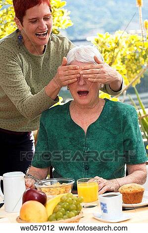 Stock Image - Elderly woman is surprised by daughter during breakfast. Fotosearch